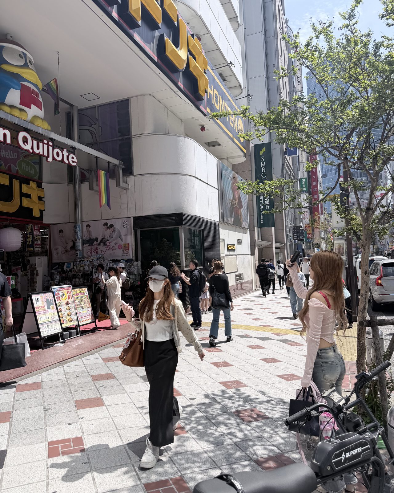 新宿のディスカウントストアの店先で、スマートフォンを掲げて外観を撮影するクリエイターの後ろ姿