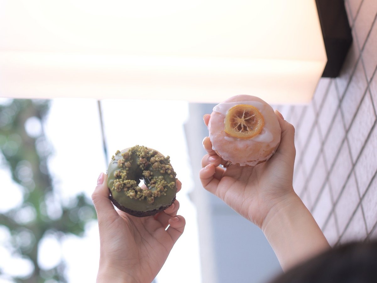 ドーナツ店の看板の下でドーナツをふたつ掲げる手